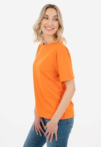 Oranžinė trumpa rankovė T-marškiniai, pagaminti iš medvilnės, su apvalia iškirpte ir sulenktomis rankovėmis, derinami su mėlynomis džinsomis.