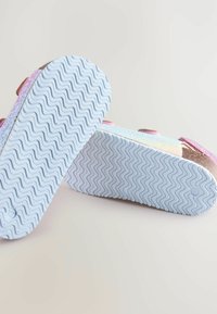 Glittriga sandaler med rosa och holografiska remmar; vit gummisula med ett vågmönster för grepp och fäste.