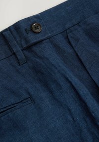Pantalons en lin bleu marine avec un devant plat, dotés d'une fermeture à bouton simple et d'une poche latérale. La texture est lisse avec des détails de tissage subtils.