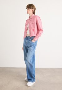 Röd och vit randig skjorta med knappar och två bröstfickor, hög midja på blå jeans och vita slip-on skor. Slät tyg och avslappnad passform.