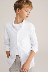 Witte button-up shirt van katoen, met een klassieke kraag, lange mouwen en een ontspannen pasvorm, gedragen over een wit T-shirt.