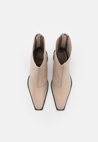 Stivali alla caviglia in pelle beige con punta appuntita, texture liscia, cerniere laterali e suola nera piatta, visti dall'alto.