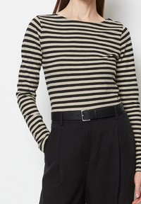 Top a maniche lunghe a righe nere e beige realizzato in tessuto morbido, con scollo a barca, abbinato a pantaloni scuri a vita alta e cintura nera.