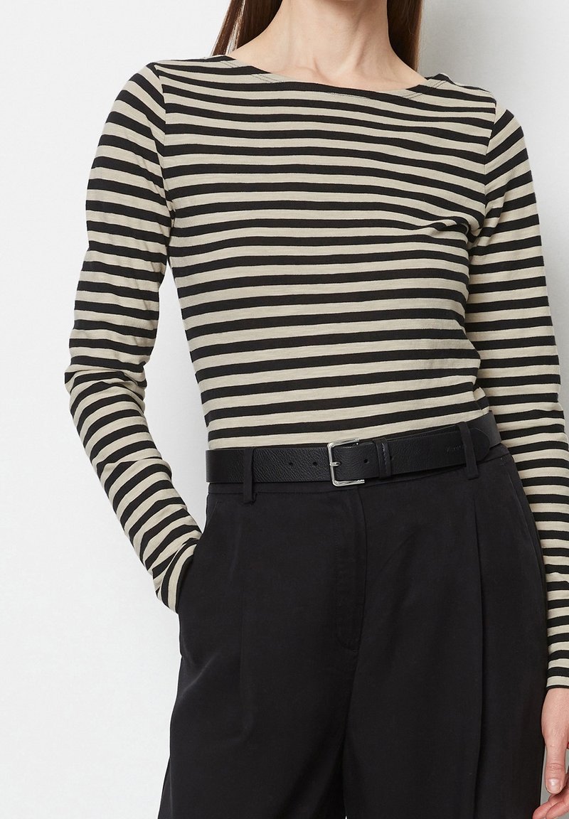 Top a maniche lunghe a righe nere e beige realizzato in tessuto morbido, con scollo a barca, abbinato a pantaloni scuri a vita alta e cintura nera.