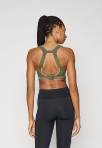 Αθλητικό σουτιέν σε ελιά πράσινο με ρυθμιζόμενους ιμάντες, σχεδιασμό racerback και κλείσιμο με αγκράφα στο πίσω μέρος. Συνδυάζεται με ψηλόμεσα μαύρα κολάν.