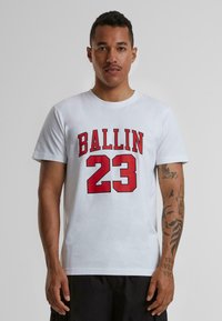 Baltas trumpas rankovės marškinėliai su ryškiu raudonu tekstu "BALLIN" ir raudonu numeriu "23", su apvalia iškirpte ir lygiu audinio tekstūru.