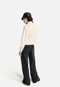 Krótka kremowa biała koszula połączona z ciemnoszarymi szerokimi jeansami. Modelka nosi czarny kapelusz typu bucket, prezentując minimalistyczny styl.