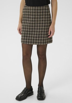 Jupe carreaux en mélange de laine de couleur marron, noir et crème. Présente une coupe ajustée, une longueur mi-cuisse et une surface texturée. Chaussures noires et collants visibles.