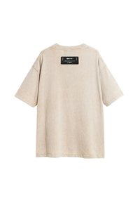 Camiseta oversized beige de mangas cortas, hecha de un tejido suave. Presenta una etiqueta negra en la parte superior de la espalda con texto. Diseño limpio y minimalista.