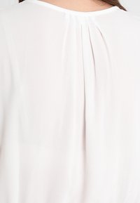 Witte blouse met een rugplooidetail, lange mouwen en een zachte, lichtgewicht stof met een gladde textuur.