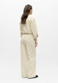 Conjunto de ropa de descanso beige que presenta una tela texturizada y ligera. La parte superior tiene un ajuste holgado con cuello, y los pantalones son de pierna ancha con cintura elástica.