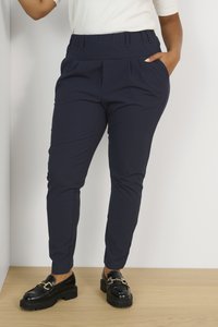 Pantaloni blu navy con una cintura larga, pieghe e tasche laterali. Abbinati a mocassini neri con dettagli in metallo dorato.