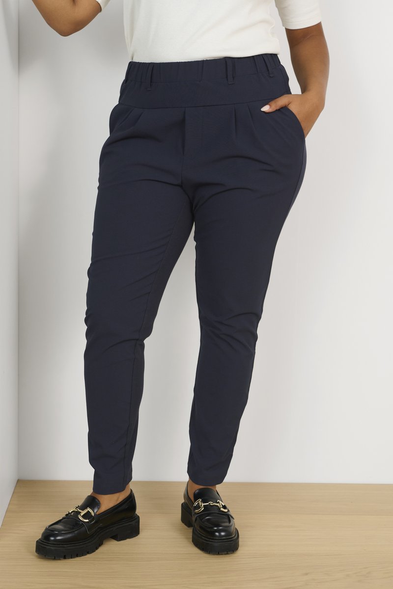 Pantaloni blu navy con una cintura larga, pieghe e tasche laterali. Abbinati a mocassini neri con dettagli in metallo dorato.