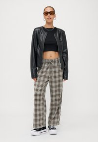 Černá koženková bunda, černý crop top, široké kalhoty s kostkovaným vzorem v hnědé a šedé barvě a černé platformové tenisky s bílou podrážkou.
