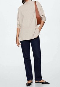 Pull en maille beige à col montant, associé à un jean droit bleu foncé et des ballerines noires pointues. Sac à bandoulière marron. Design minimaliste.