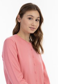 Rožinis kardiganas, pagamintas iš minkštos medžiagos, su apvalia iškirpte ir šešiais mygtukais priekyje. Ilgos rankovės su raukiniais.