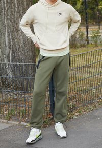 Beige fläckig hoodie med framficka och dragsnören, parat med olivgröna sweatpants med dragkedjefickor, bärs med vita sneakers.