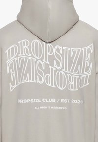 Lys grå hoodie med et stort hvidt tekstdesign, der læser "DROPSIZE" og "DROPSIZE CLUB / ETAB. 2020" på ryggen. Blødt stof.