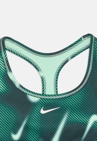 Nike sportmelltartó zöld és fekete csíkos mintával, nyitott hátú kialakítással és világosabb mentazöld díszítéssel.