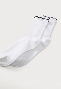 White socks with a ruffled black trim at the top, made from a smooth, stretchy fabric. They have a classic crew length and lightweight texture.
