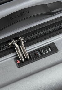 Valigia argentata con un'esterno liscio, doppia cerniera con hardware nero e un pannello con combinazione approvato TSA.