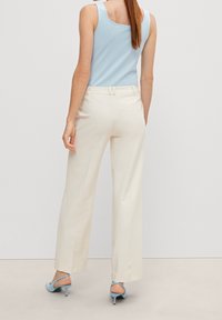 Breda ben i krämfärgade byxor med en slät textur och bältesdetalj, kombinerat med en ljusblå ärmlös topp och ljusblå klackar.