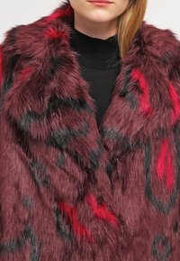 Chaleco de piel sintética en burdeos profundo con patrones abstractos en negro y rojo. Textura suave con una apariencia gruesa y mullida, diseñado para ofrecer calidez.