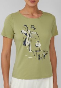 Olijfgroene t-shirt met een ronde halslijn en korte mouwen, featuring een zwarte lijntekening van twee vrouwen en een hond.
