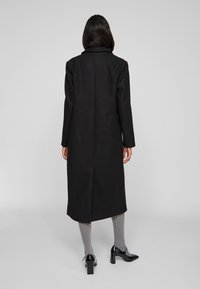 Must mustat pikkjope sirge lõike, nurgelise kraega ja pikkade varrukatega. Kombineeritud hallide retuuside ja mustade platvormikontsadega kingadega.