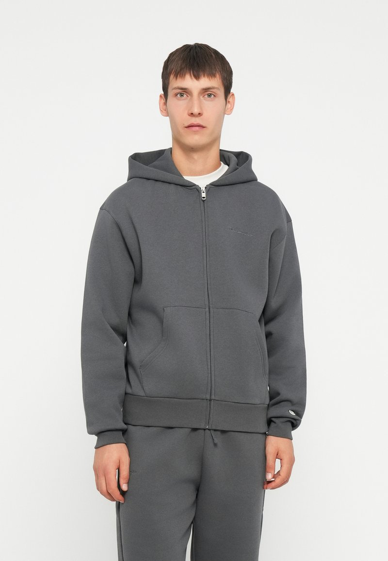 Felpa grigia con zip, dotata di un ampio cappuccio, tasche frontali e polsini a costine. Presenta un piccolo logo ricamato sul petto. Tessuto in misto cotone.