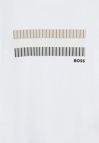 Maglietta bianca con grafica di tasti di pianoforte nei toni del nero, beige e bianco. Nome del marchio "BOSS" stampato in nero sul fondo.