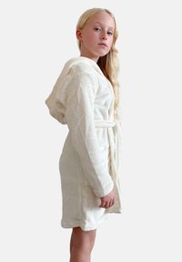 Hvid hættebadekåbe lavet af blødt, luksuriøst stof. Funktioner en bæltestrop i taljen, sidelommer og en struktureret overflade.