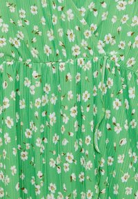 Tissu vert avec un imprimé floral blanc et jaune, présentant une taille froncée et des plis verticaux.