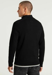 Maglione nero a maglia con colletto alto, caratterizzato da un tessuto testurizzato, maniche lunghe e un sottile dettaglio del logo sul retro.