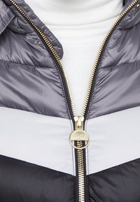 Padded jacket featuring a colorblock design in grey, white, and black. Gold zipper closure with a round pull tab. Textured fabric.