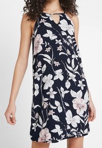 Blommig klänning i marinblått tyg med rosa och vita blommor, design med halterneck och en front med nyckelhålskärning, samt lös passform.