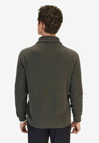 Mörkgrön ribbad stickad tröja med hög krage, sänkt axel och åtsittande manschetter. Texturen verkar mjuk med ett subtilt mönster.