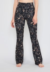 Leggings acampanados negros con un patrón texturizado de serpiente y flores en tonos de beige y crema. Diseño de cintura alta con una banda elástica.
