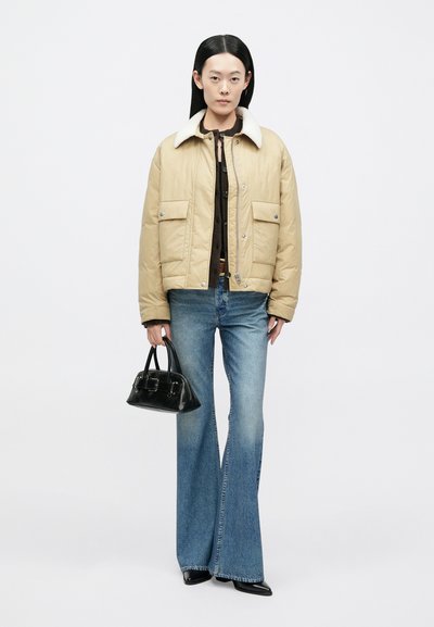 Beež pufferjakk lambanahast kraega, sinised laiade säärega teksad ja väike must käekott, millel on sile tekstuur ja metallist detailid.