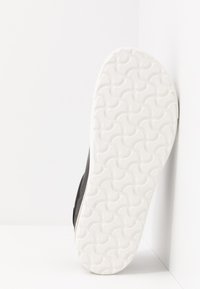 Sneaker nera con tomaia testurizzata e suola in gomma bianca con un motivo ondulato. Posizionata su uno sfondo bianco.