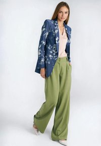 Niebieska marynarka w kwiatowy wzór noszona na blado różowej bluzce, z zielonymi spodniami o szerokich nogawkach i jasno różowymi szpilkami. Gładkie tekstury i dopasowany krój.