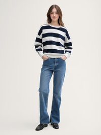 Marinblå och vit randig sweatshirt med rund halsringning, oversized passform, tillsammans med ljusblå utsvängda jeans och svarta skor.
