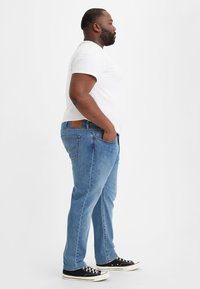 Jeans de mezclilla azul claro con corte recto, llevados en la cintura, cuentan con cinco bolsillos y un parche de cuero marrón en la parte trasera.