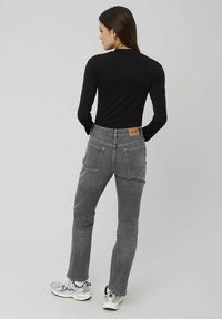 Jean en denim gris avec une coupe droite, présentant une étiquette en cuir à l'arrière et des coutures discrètes. Associé à un haut noir ajusté à manches longues.