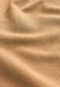 Tissu en coton beige présentant une surface texturée avec de légères plis et un motif de tissage uniforme. Aucun motif ou accent distinct visible.