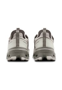 L'immagine mostra un paio di scarpe sportive grigie con una tomaia testurizzata, un tallone imbottito e una suola in gomma distintiva con scanalature profonde.