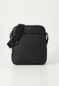 Sort læder skuldertaske med struktureret overflade, justerbar rem, lynlås lukning foroven og lynlåslomme foran. Kompakt, firkantet form.