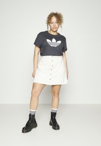 Juodas marškinėliai su baltu Adidas logotipu, kreminis mygtukinis sijonas, juodi raišteliais batus ir juodai baltas juostuotas kojines. Paprasta fono.