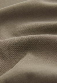 Tela caqui con una superficie suave y texturizada, que muestra un ribeteado fino y consistente y un caído suave. Detalles de color y material claros y evidentes.