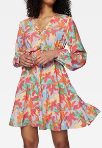 Robe florale colorée avec des manches longues, un col froncé, une jupe à volants et des motifs vibrants orange, rose, vert et bleu sur un fond clair.